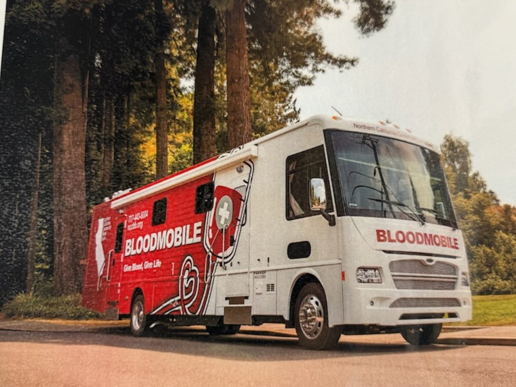 The modern Northern California Community Blood Bank Bloodmobile parked among the redwoods
