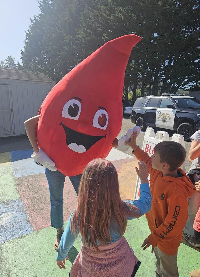 Buddy the blood-drop mascot high-fiving children at a community event